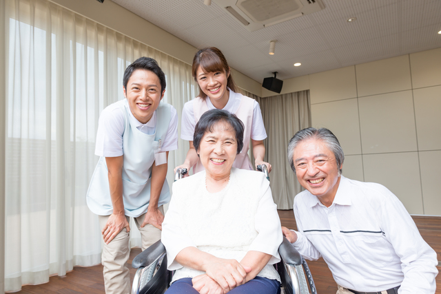 介護施設の前で微笑む利用者夫婦と介護職