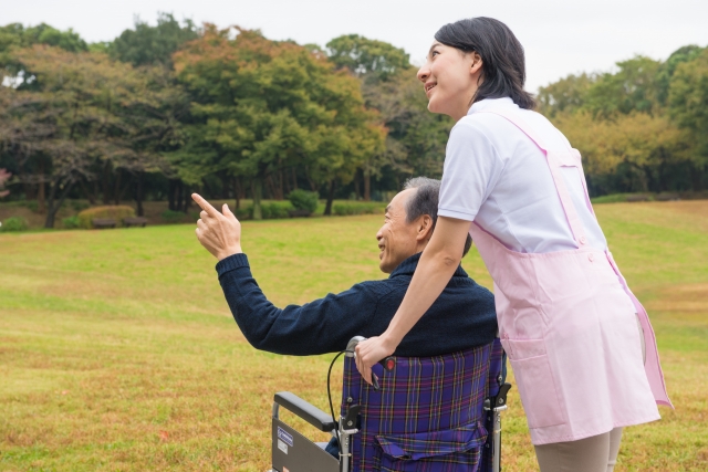 高齢者の車椅子を押して公園を散歩する介護職の女性