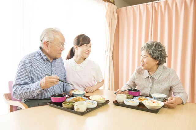 グループホームで食事を食べる介護職と利用者